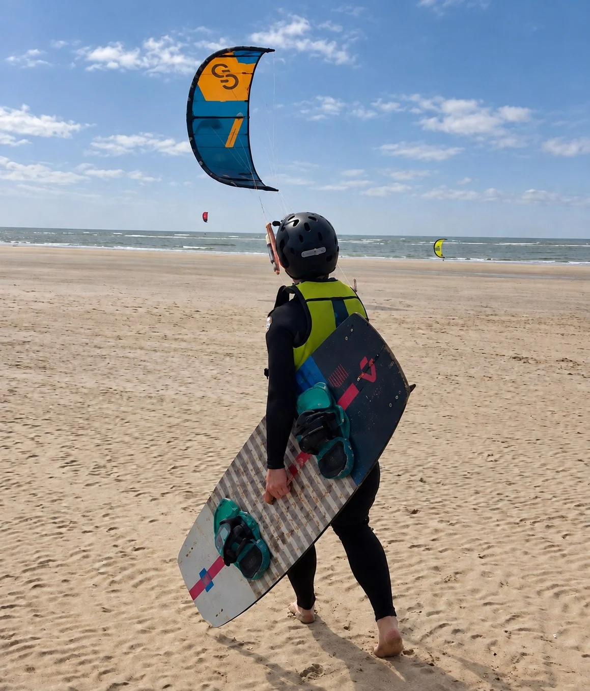 Kitesurfer carrying a board beneath a kite on the beach